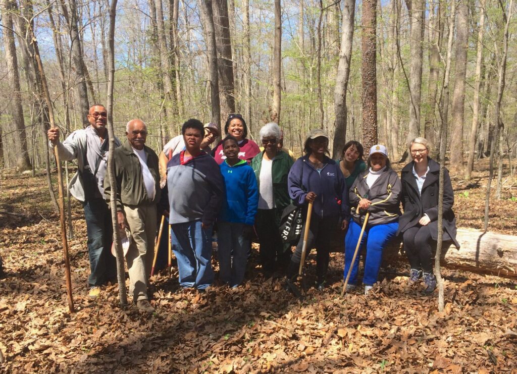 Intergenerational, mixed gender group of African Americans and two white feminine-presenting people posing together in the woods for a group photo