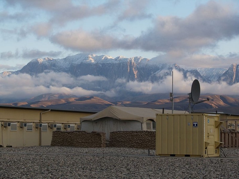 Military tents and barracks and satellite overlooking a landscape of mountains and clouds with the sun shining down on them