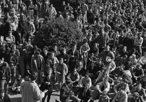 dc.lib.unc Crowd of majority white-presenting students gathering to listen to a speaker on the grounds of UNC campus. The speaker is standing on the front steps of a campus building